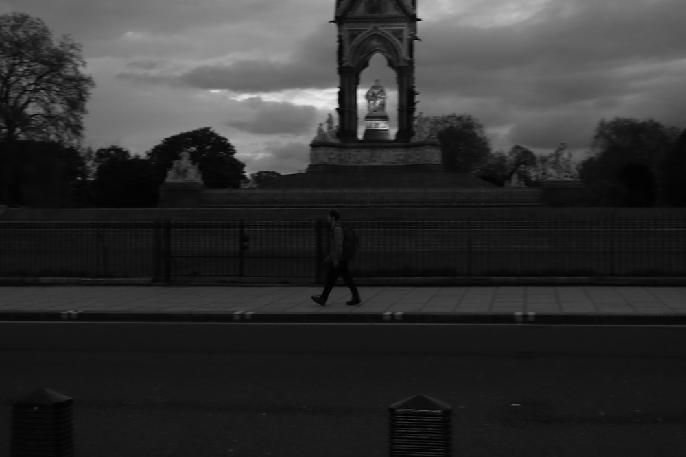 Una foto en blanco y negro de un hombre caminando frente a una torre del reloj