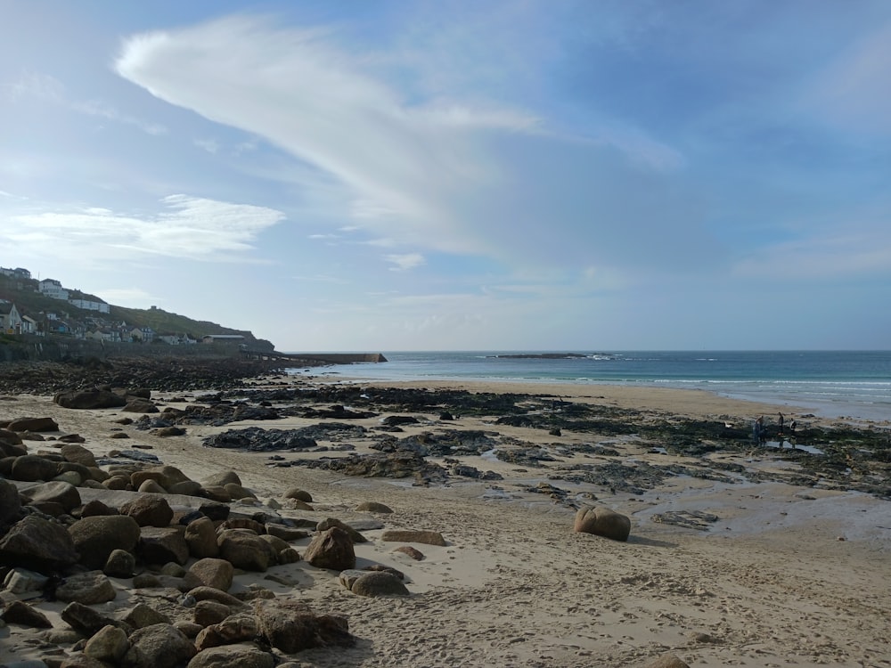 a sandy beach with rocks and houses in the background