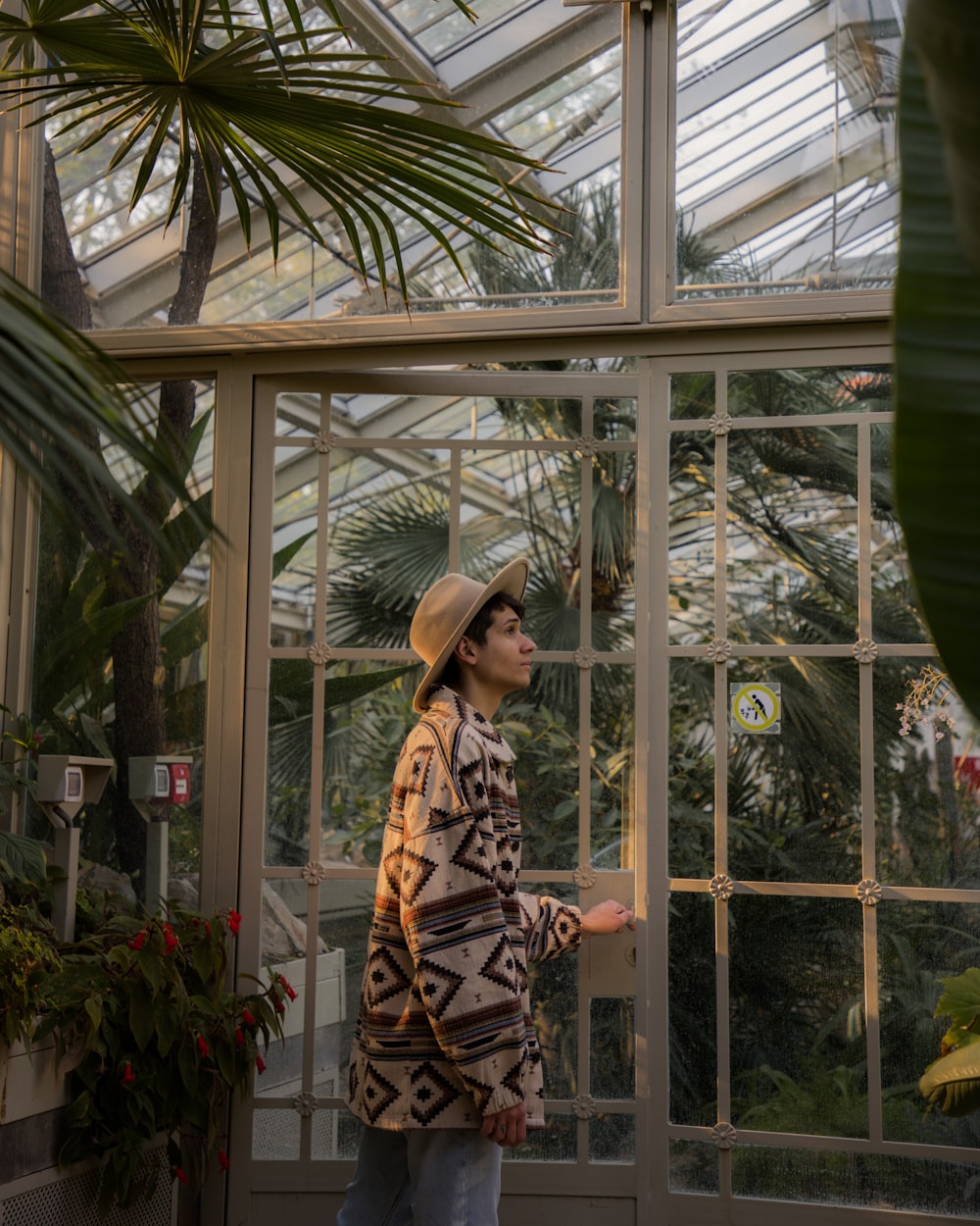 a woman in a hat standing in a greenhouse