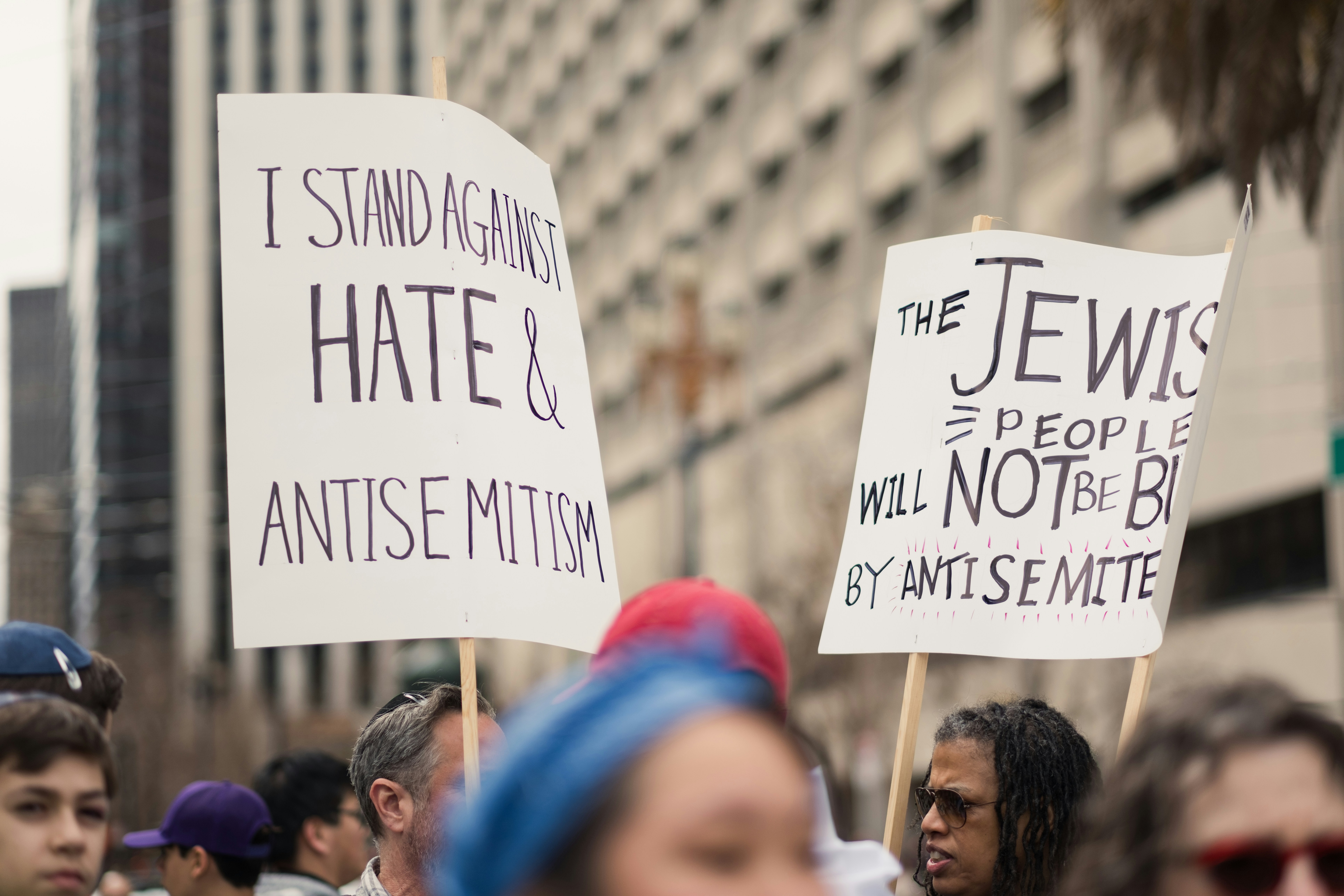 a group of people holding signs in the street, People hold up signs stating "I STAND AGAINST HATE & ANTISEMITISM" AND "THE JEWISH PEOPLE WILL NOT BE BULLIED BY ANTISEMITES" at the Unity Rally, a march against antisemitism in San Francisco.