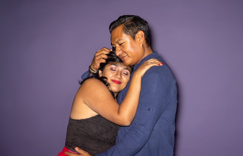 a man and woman embracing each other in front of a purple wall