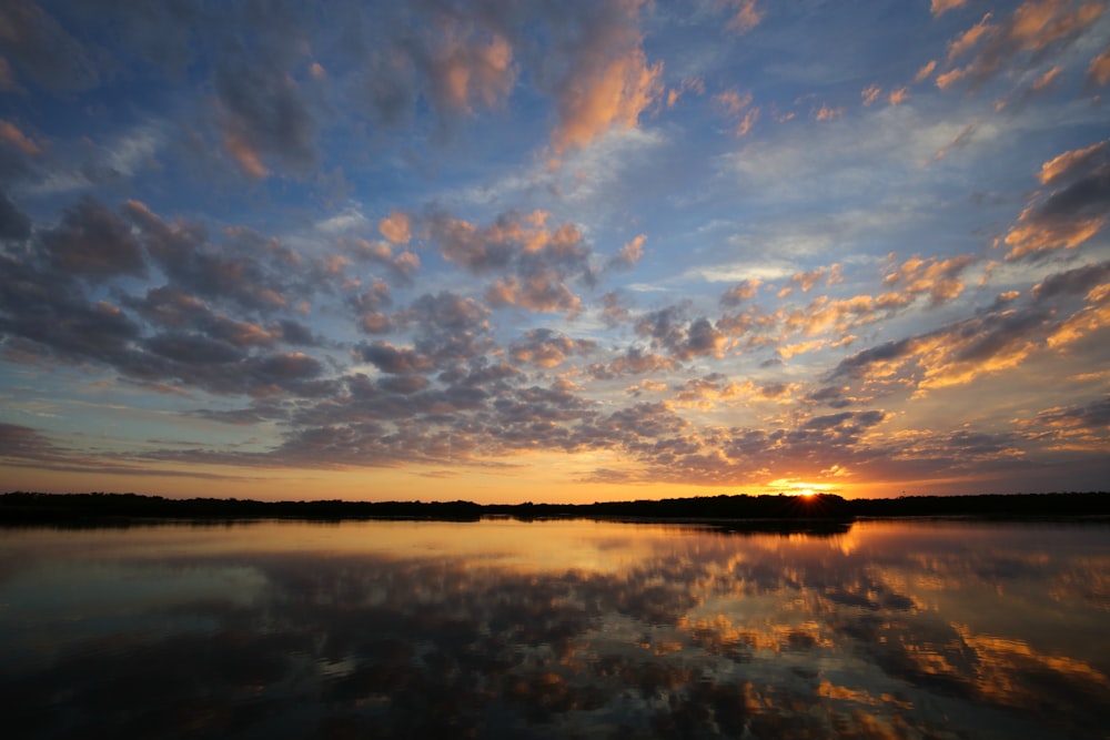 the sun is setting over a calm lake