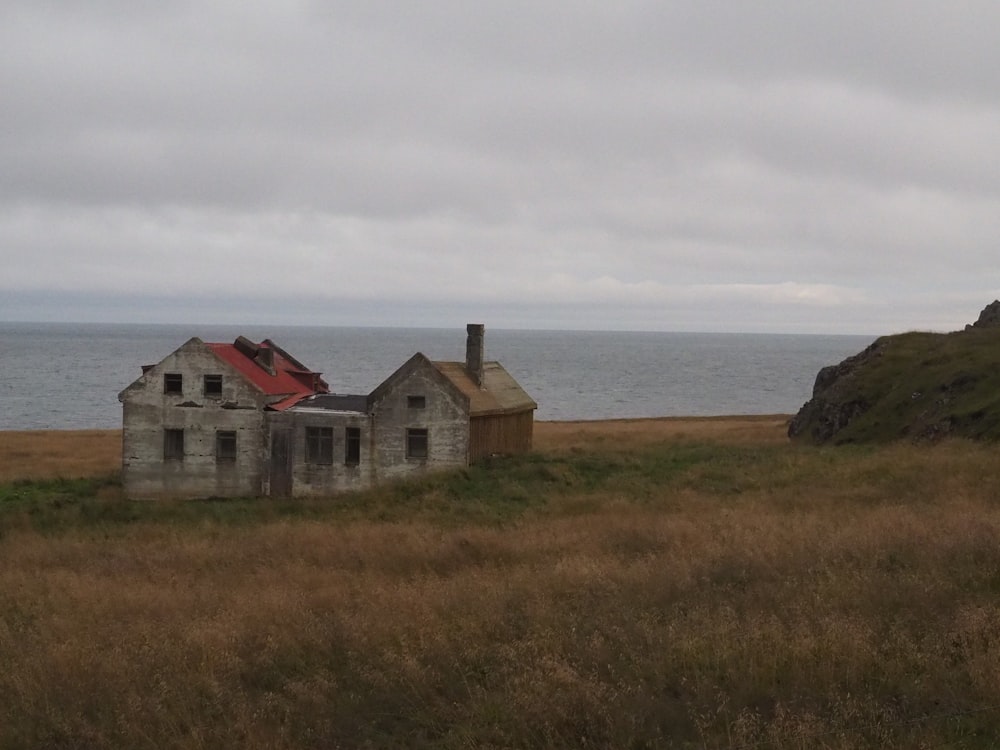 an old abandoned house sitting in a field next to a body of water