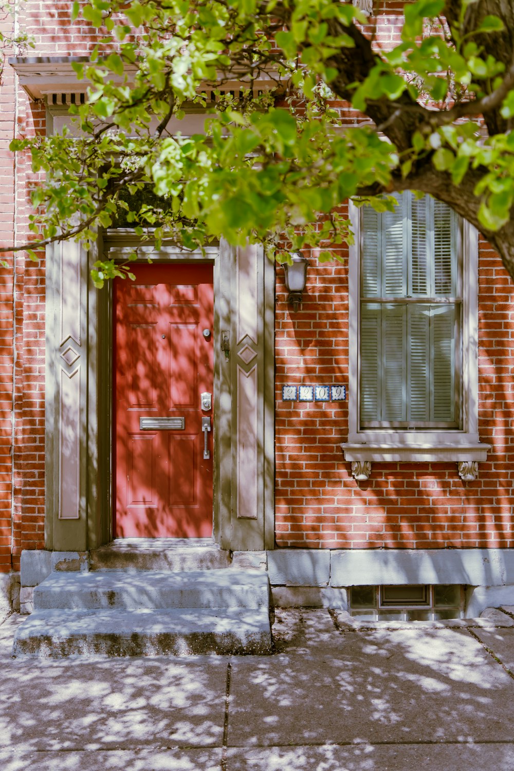 a brick building with a red door and a tree