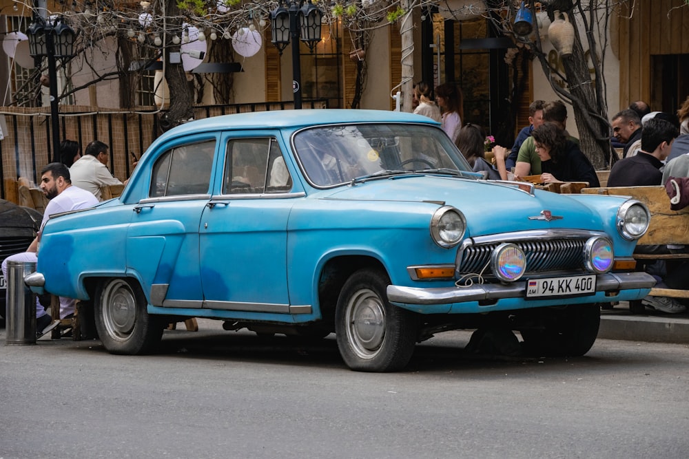 an old blue car parked on the side of the road