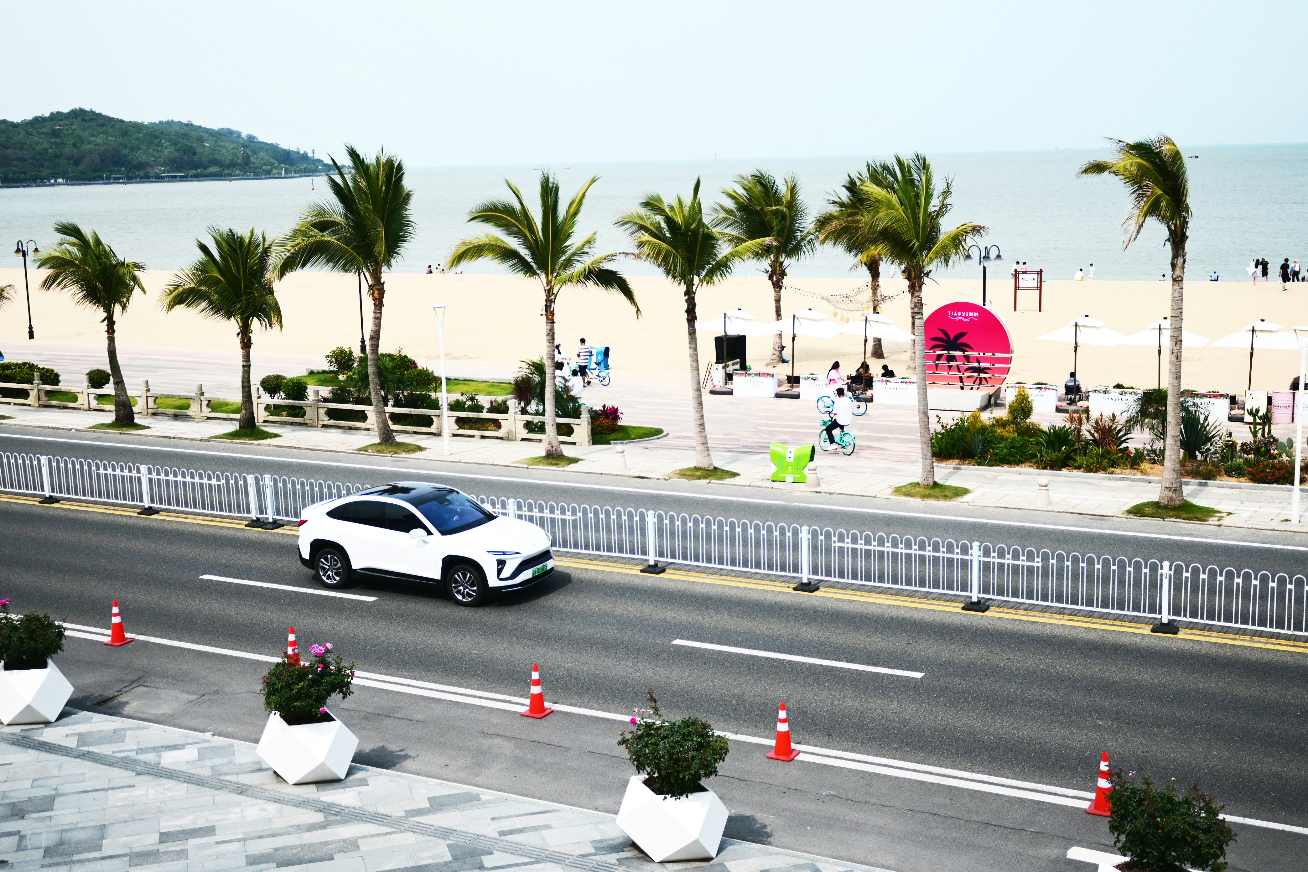 a white car driving down a street next to a beach