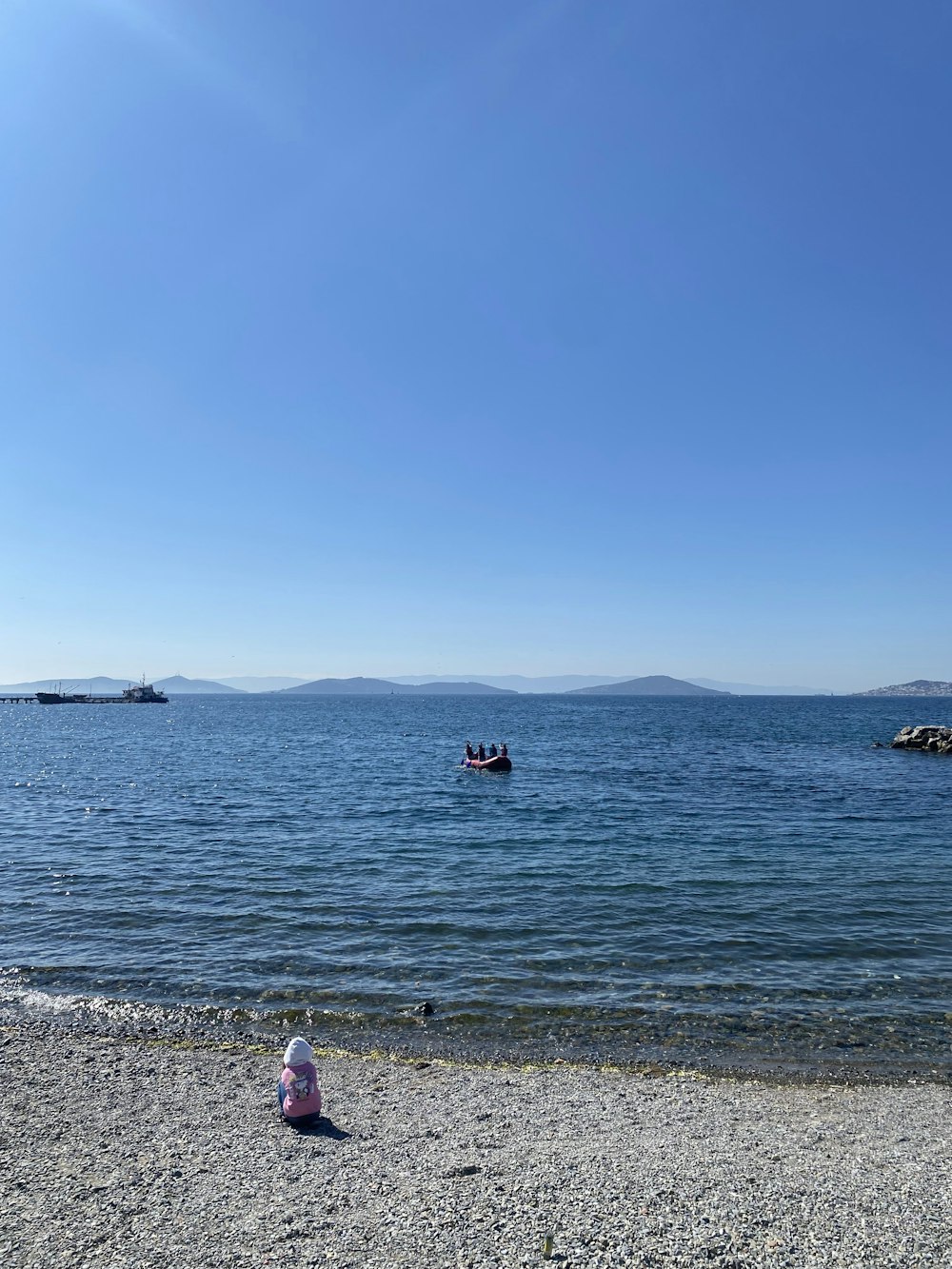 a small child sitting on a beach next to a body of water