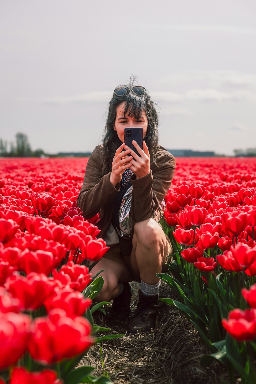 a woman taking a picture of herself in a field of red tulips
