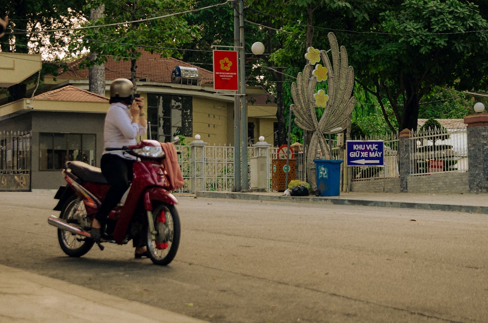 a woman riding a red motorcycle down a street