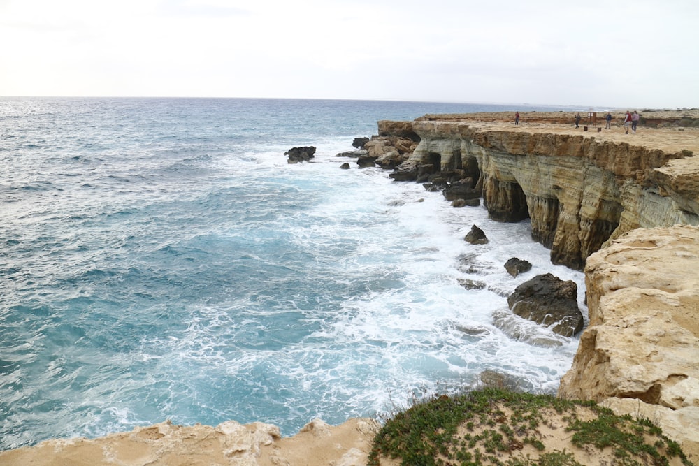 people are standing on the edge of a cliff by the ocean