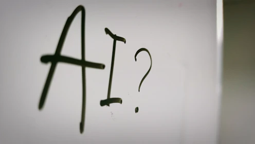 The letters AI and a question mark written in black marker on a whiteboard