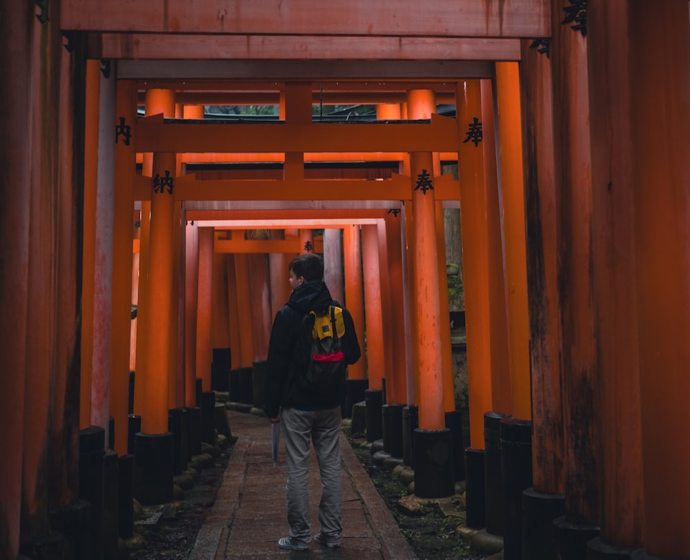 a man with a backpack walking through a tunnel of orange tori tori tori tori tori