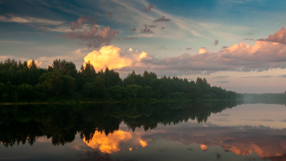 a body of water surrounded by trees and clouds
