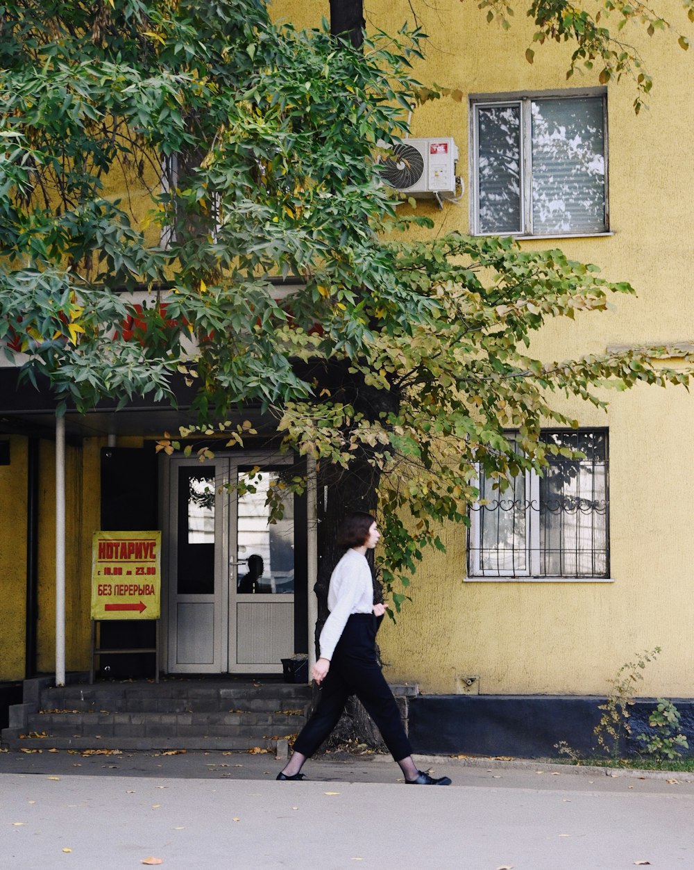 a woman walking down a street past a yellow building