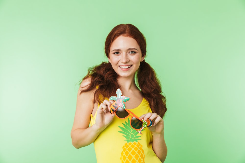 a woman in a yellow shirt is holding a pineapple
