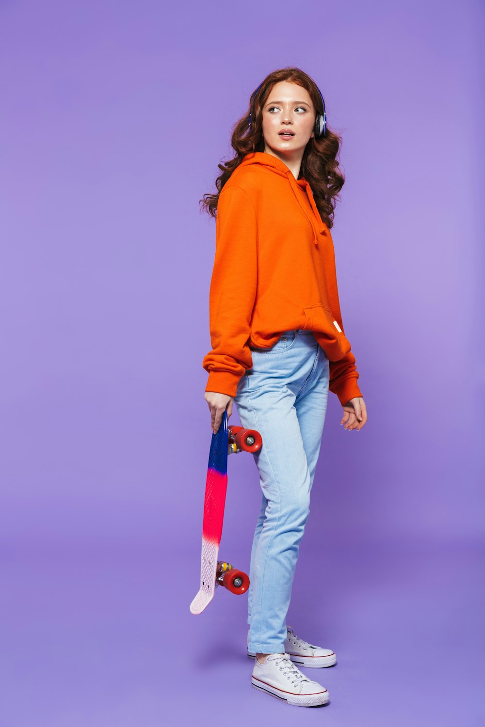 a woman in an orange hoodie holding a skateboard