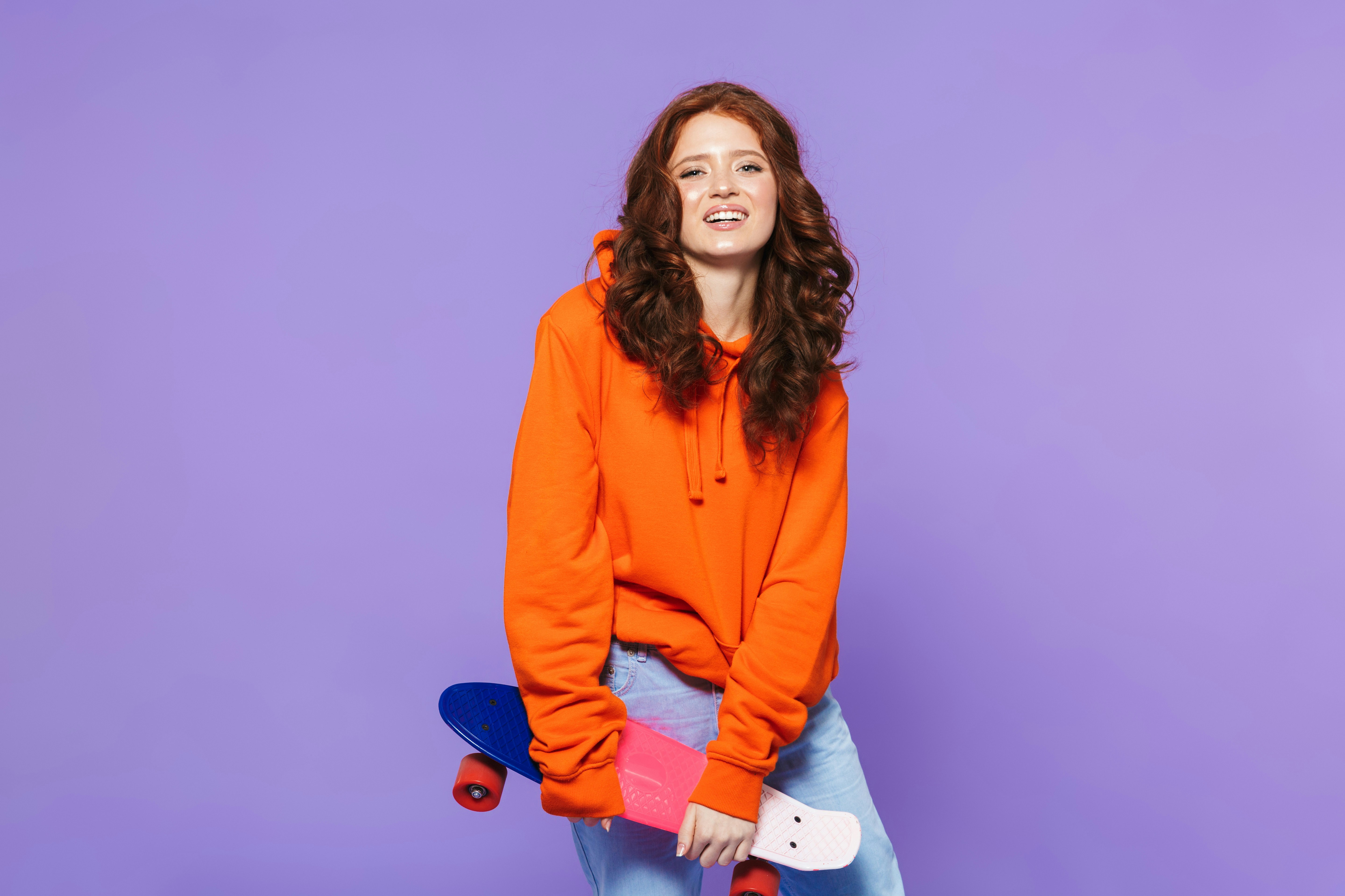 a woman in an orange sweatshirt holding a skateboard