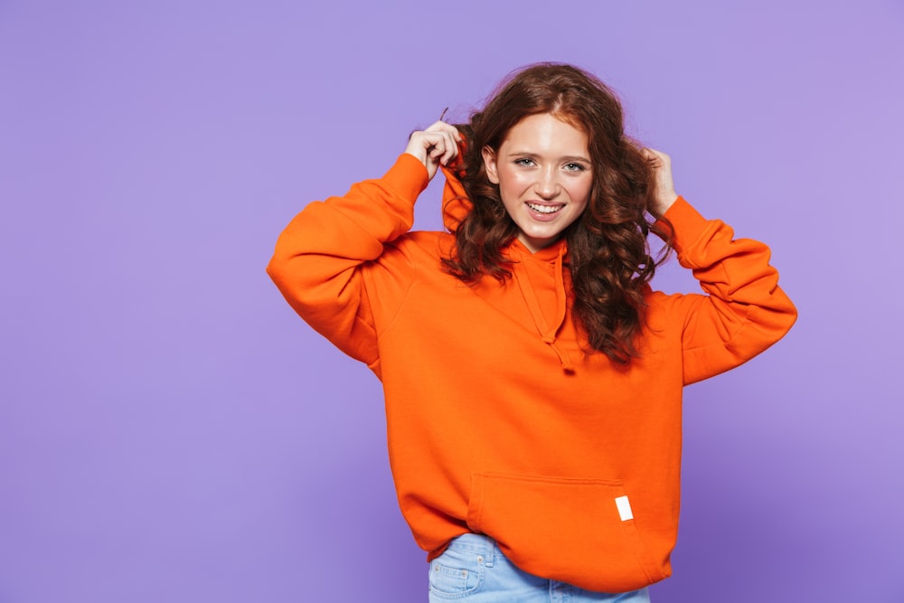a woman in an orange hoodie poses for a picture
