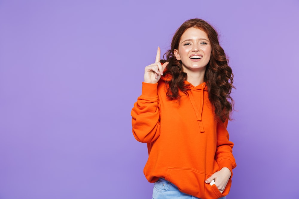 a woman in an orange hoodie pointing up
