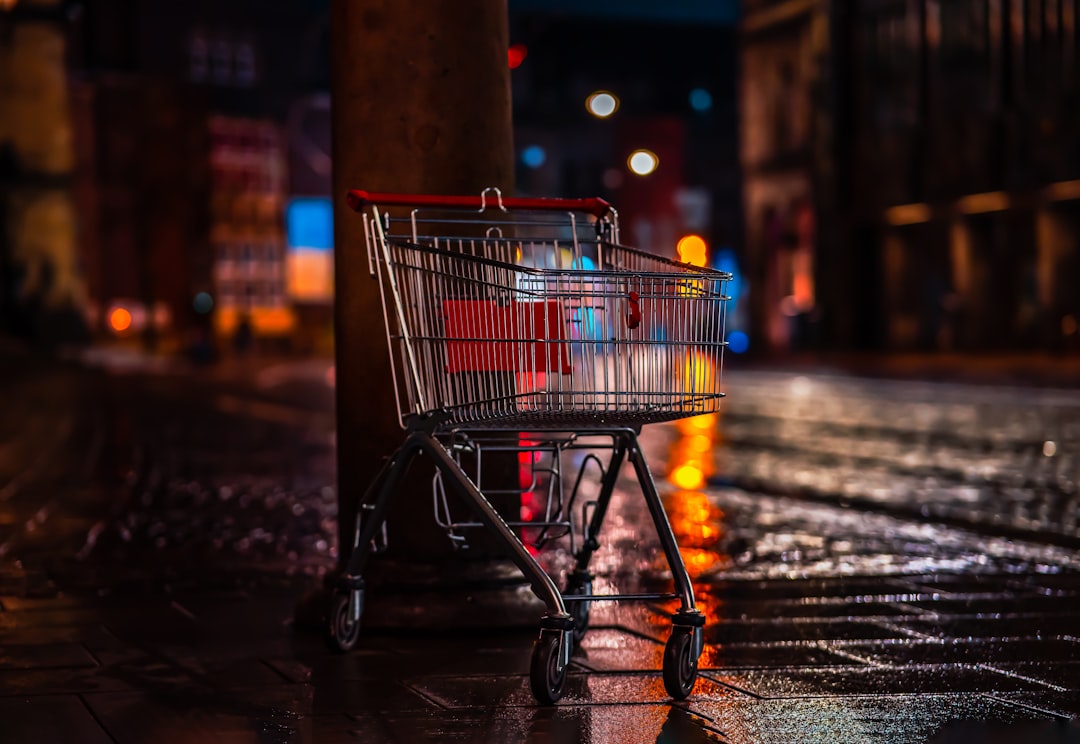 a shopping cart sitting next to a pole on a wet sidewalk, A shopping cart sits on a tiled floor on a dark street.
