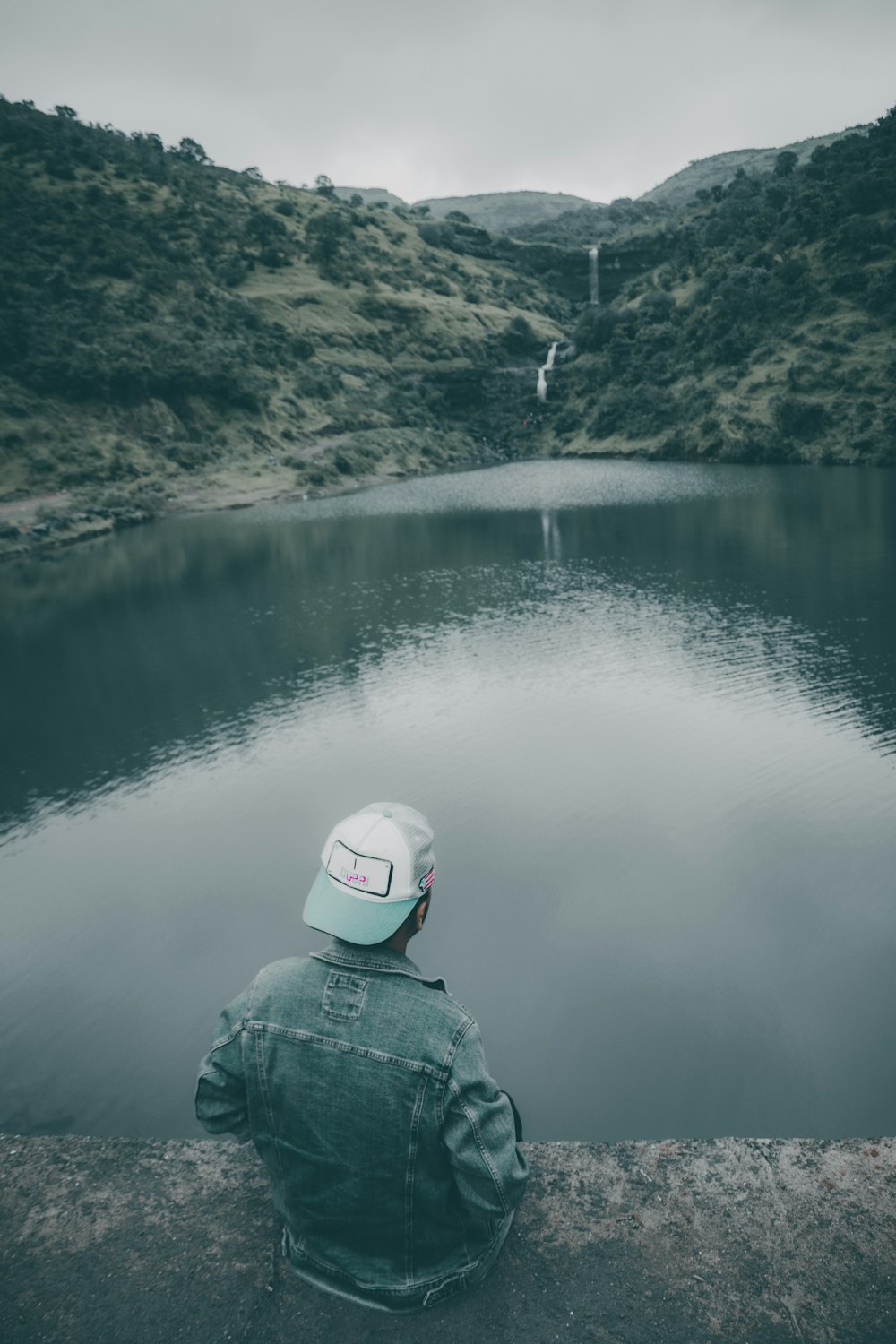 a person sitting on a ledge looking at a body of water