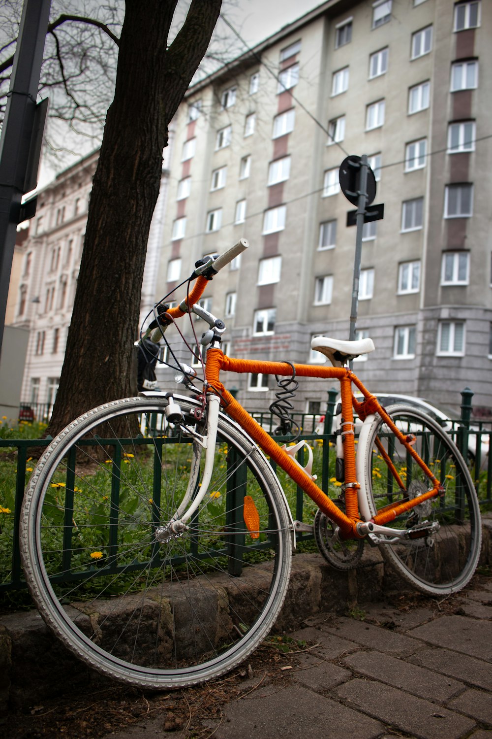 an orange and white bicycle parked next to a green fence