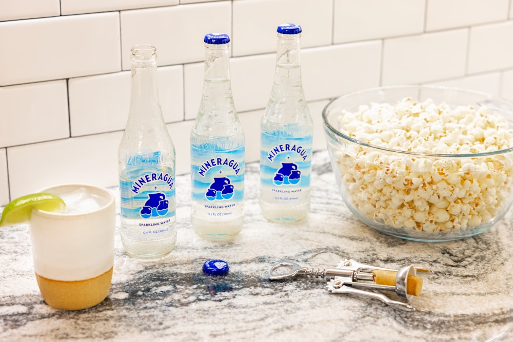 a bowl of popcorn, two bottles of water, and a glass of water