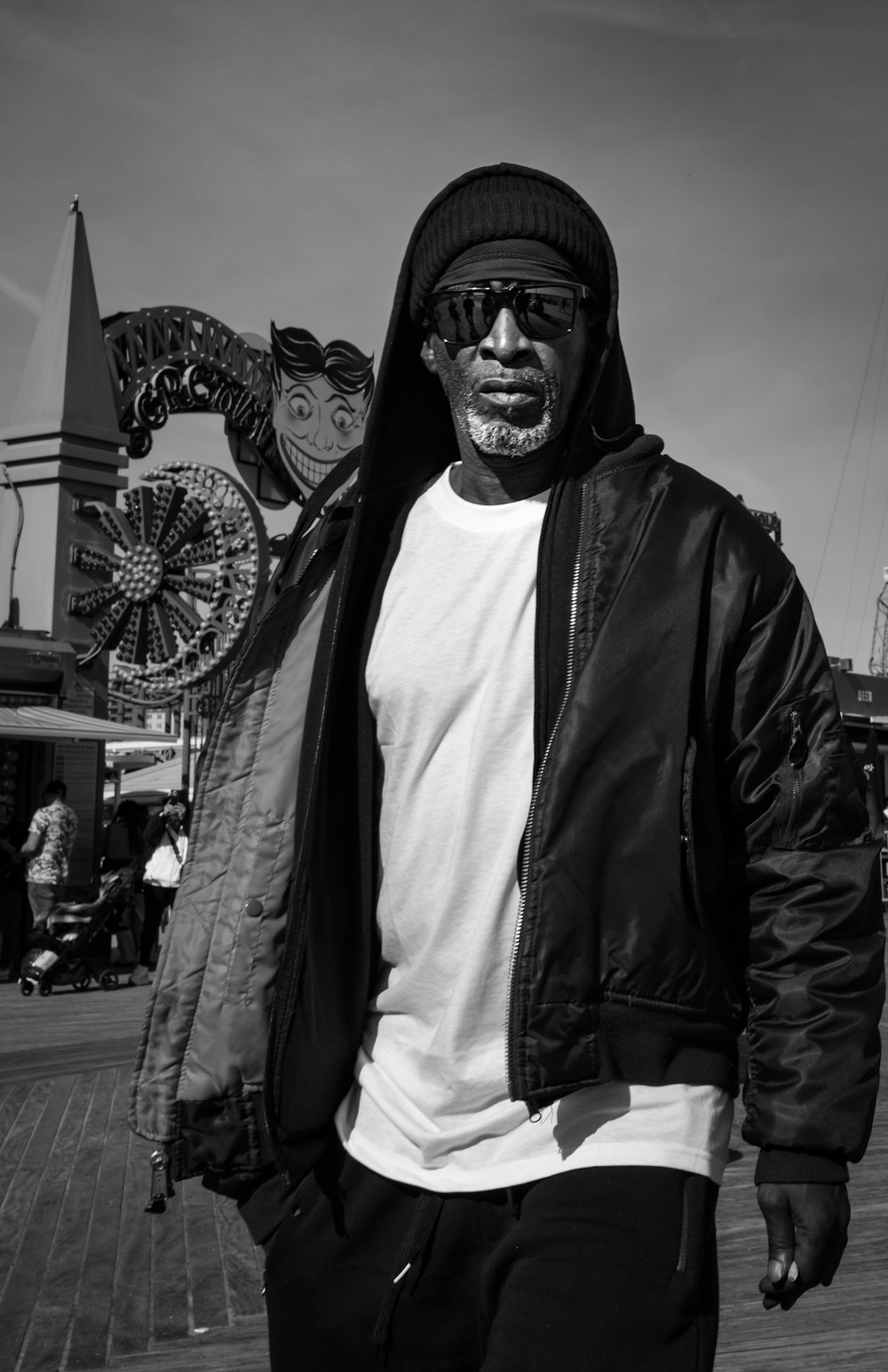 a man in a jacket and sunglasses standing on a boardwalk