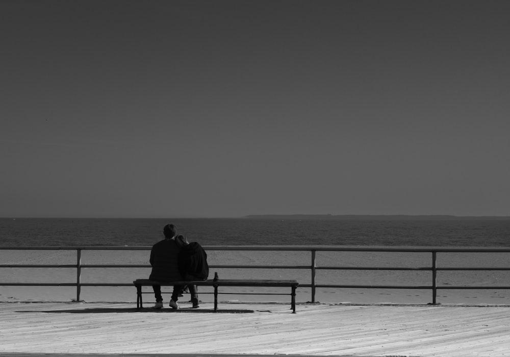 two people sitting on a bench looking out at the ocean