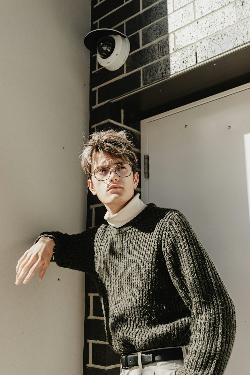 a man wearing glasses leaning against a wall