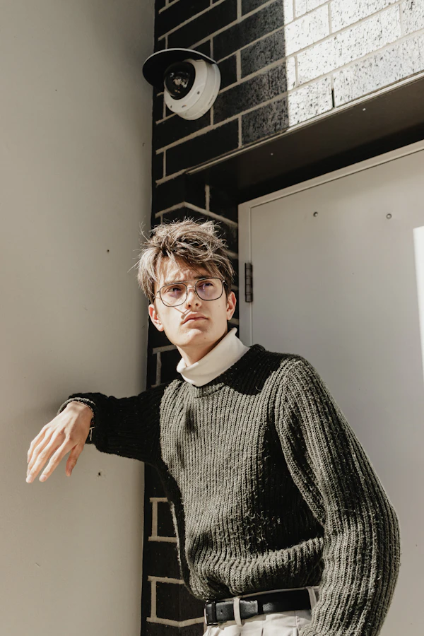 Man in knitwear and glasses by a wall