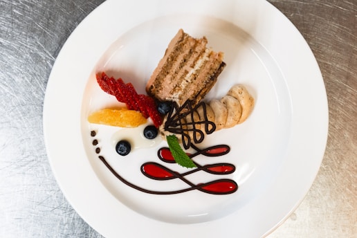 a white plate topped with a piece of cake and fruit