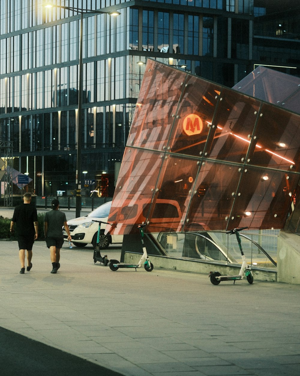 two people walking down a sidewalk next to a tall building