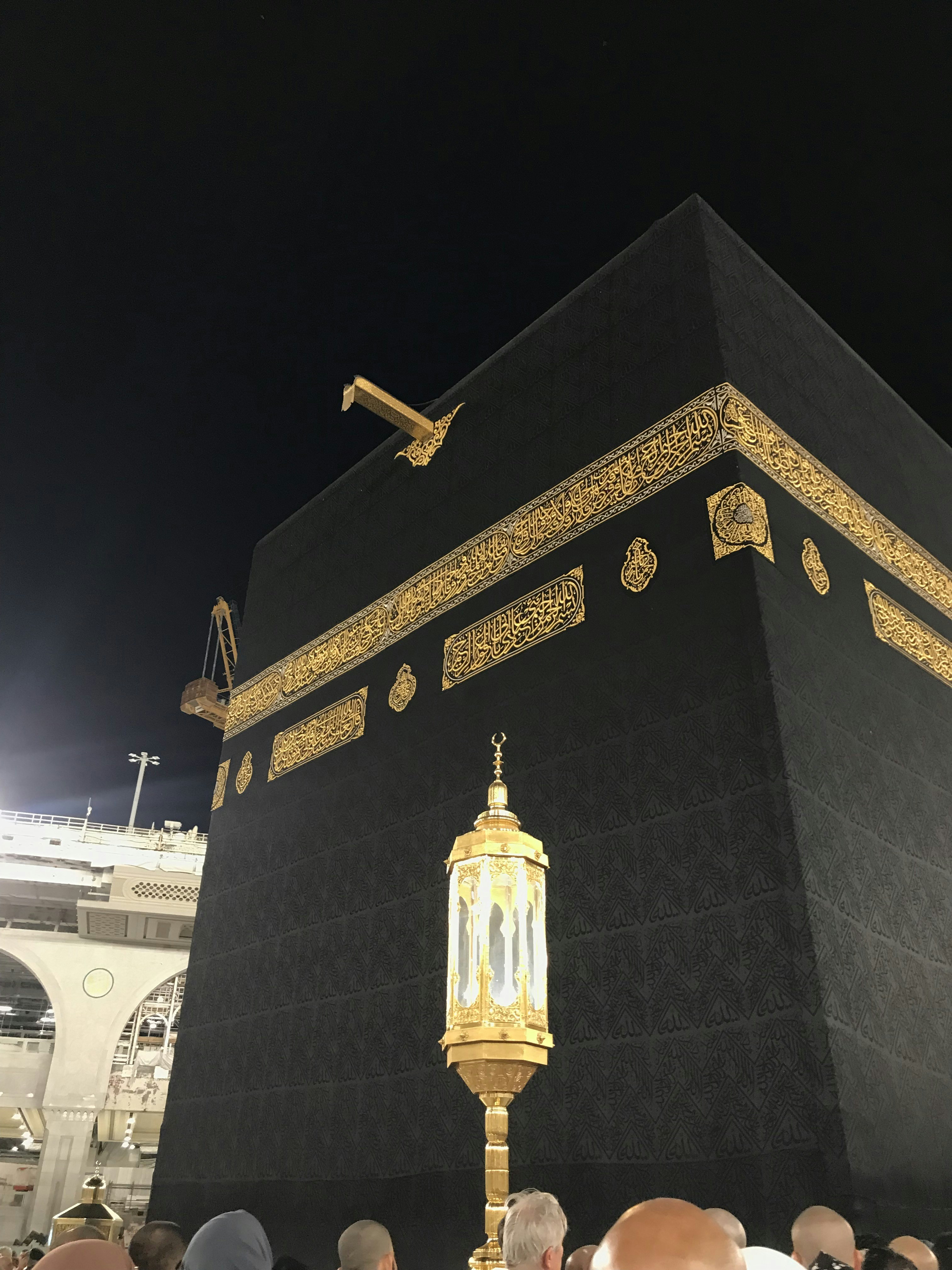 Kaaba at Masjid al-Haram illuminated at night with dark sky and thousands of pilgrims