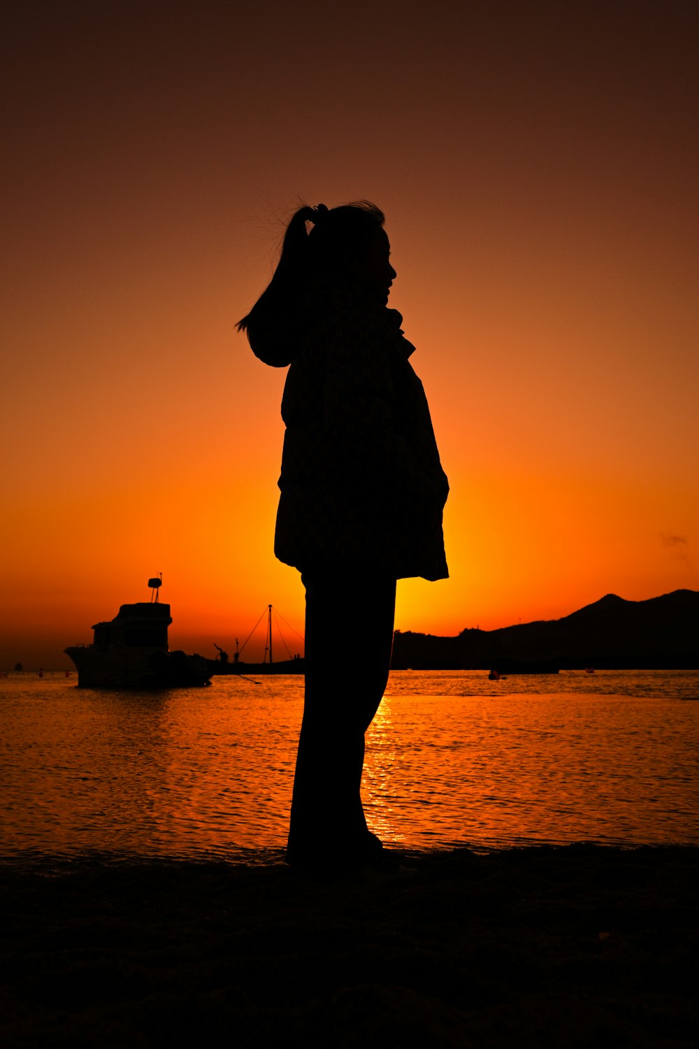 a person standing in front of a body of water at sunset