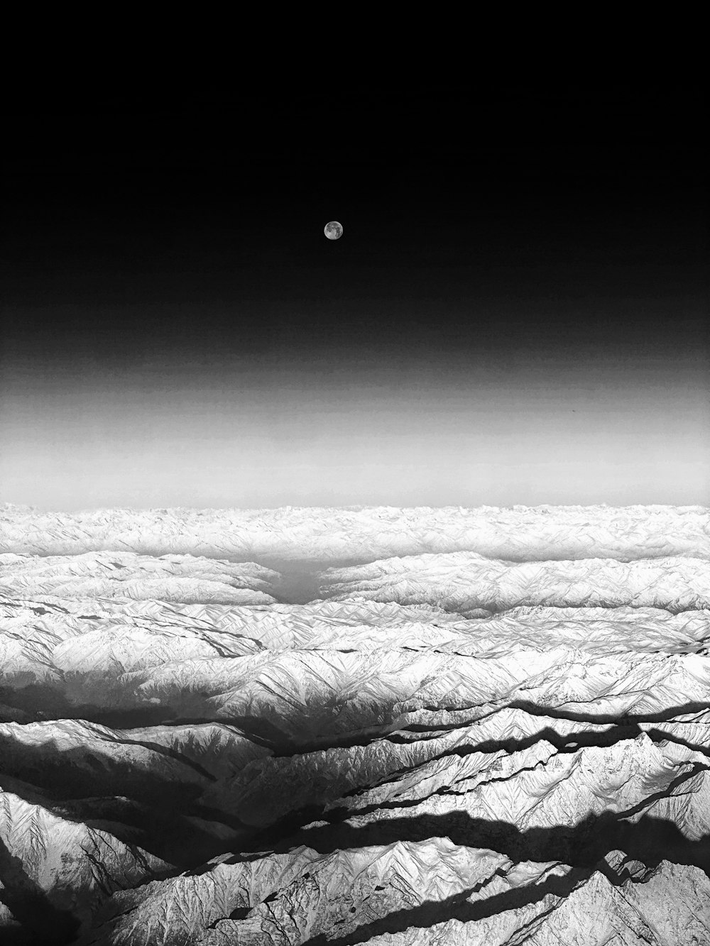 a black and white photo of mountains and a moon
