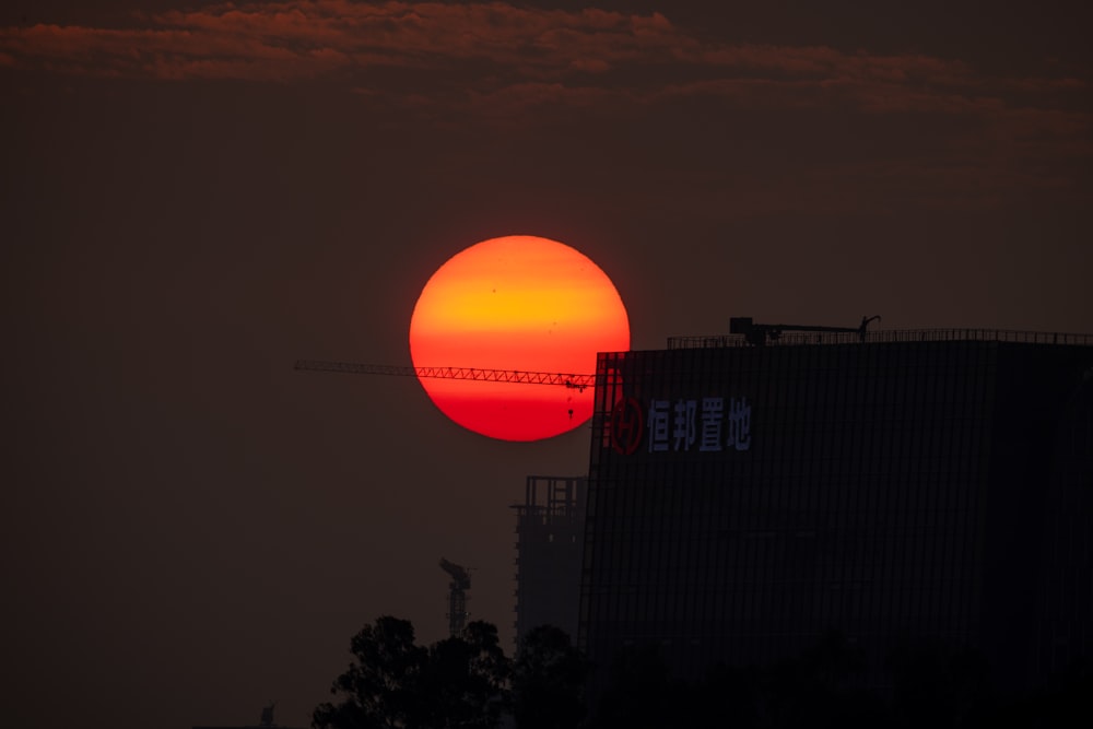the sun setting behind a building with a crane in the foreground