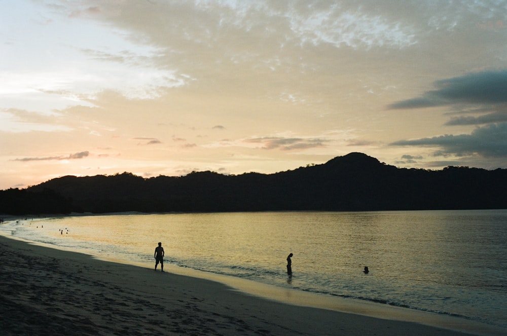 a couple of people standing on top of a sandy beach