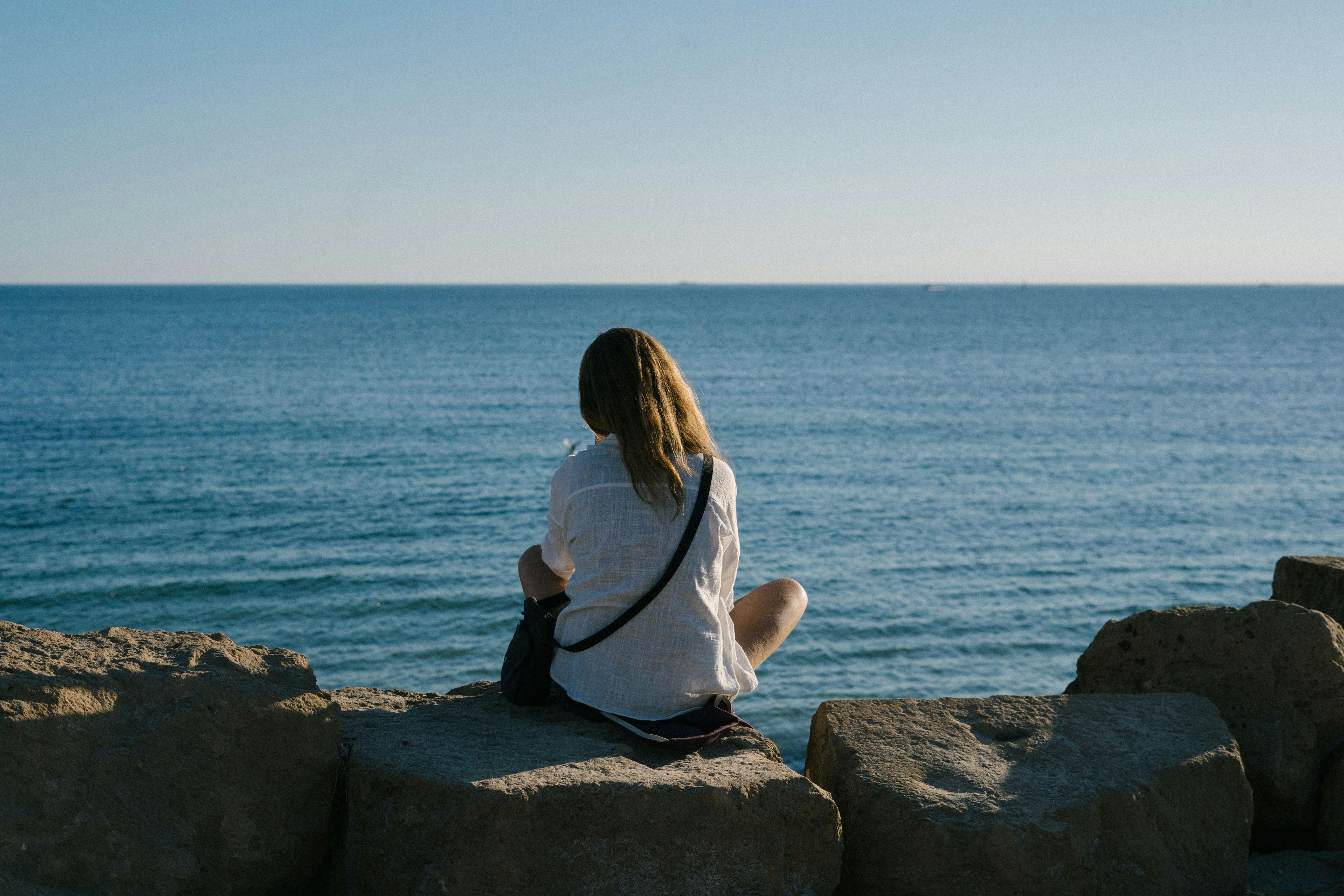 a woman sitting on a rock looking out at the ocean