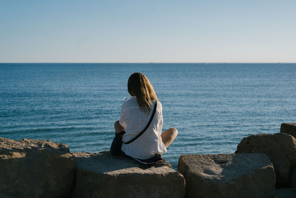 a woman sitting on a rock looking out at the ocean