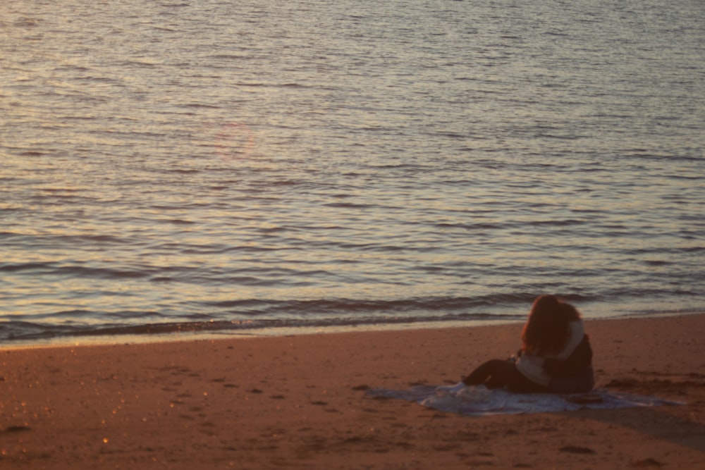 a woman sitting on a beach next to the ocean