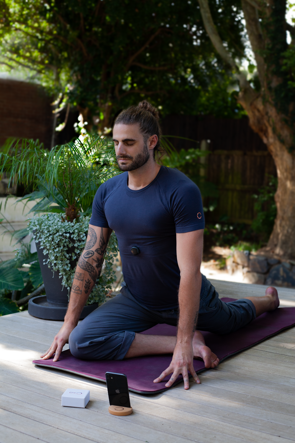um homem sentado em um tapete de ioga no meio de um jardim