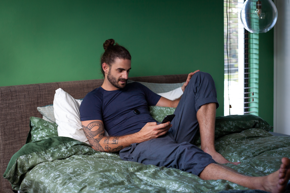 um homem sentado em uma cama olhando para seu celular
