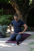 a man sitting on a yoga mat with his hands in his pockets