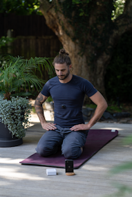 a man sitting on a yoga mat with his hands in his pockets