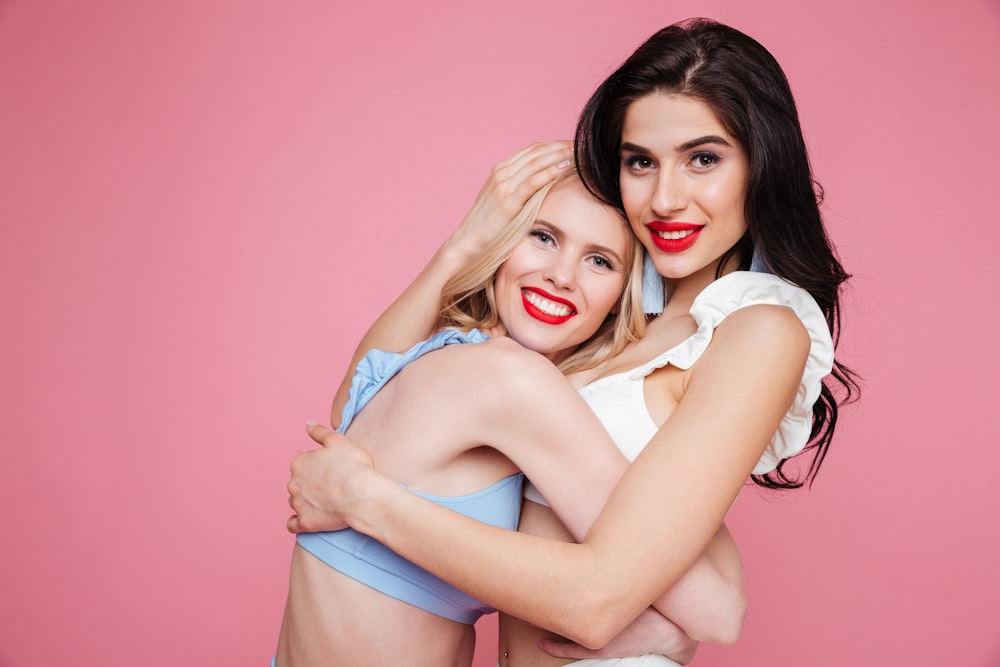 two beautiful women hugging each other in front of a pink background