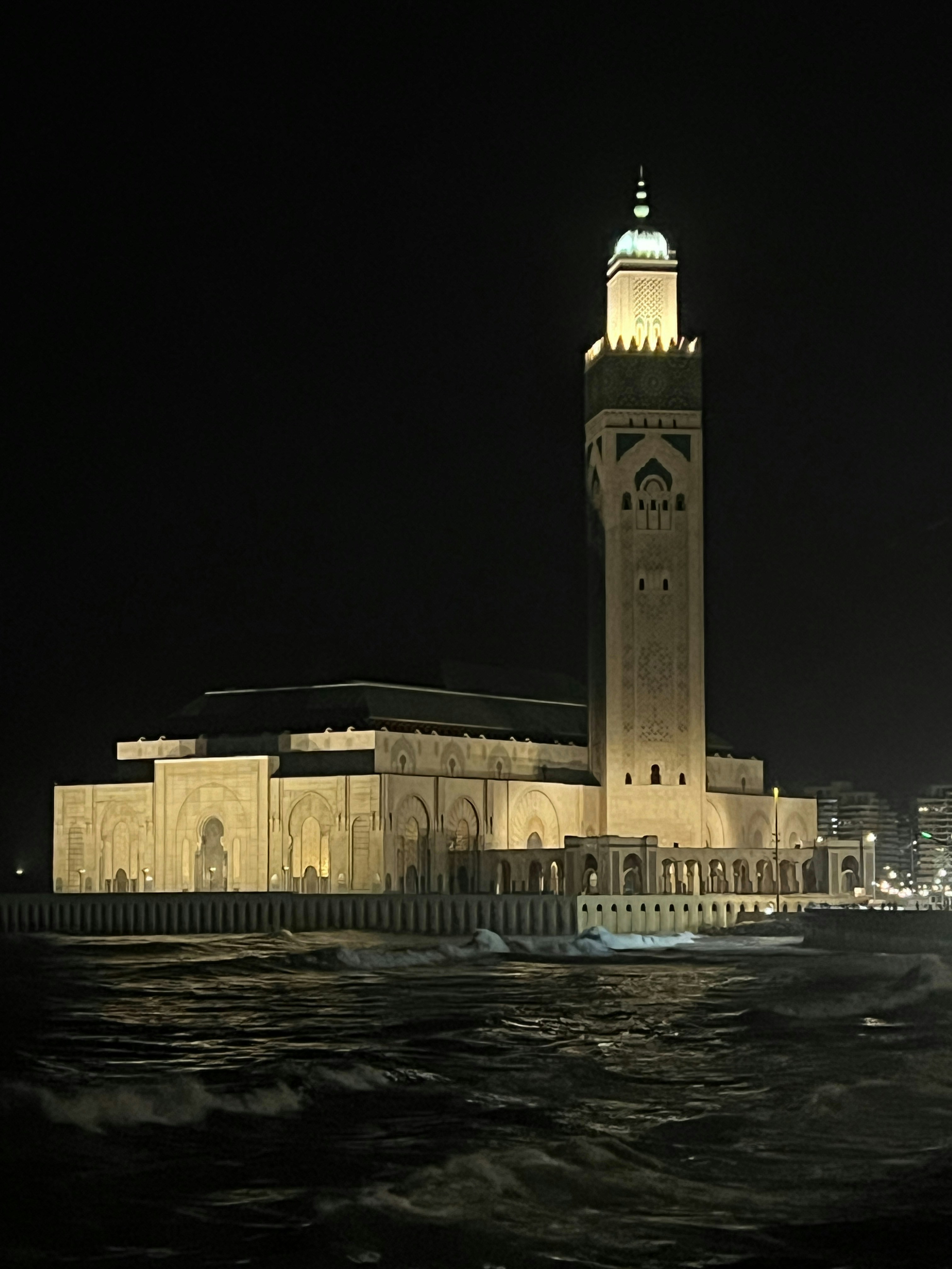 Hassan II Mosque in Casablanca at night with illuminated minaret reflecting in the ocean