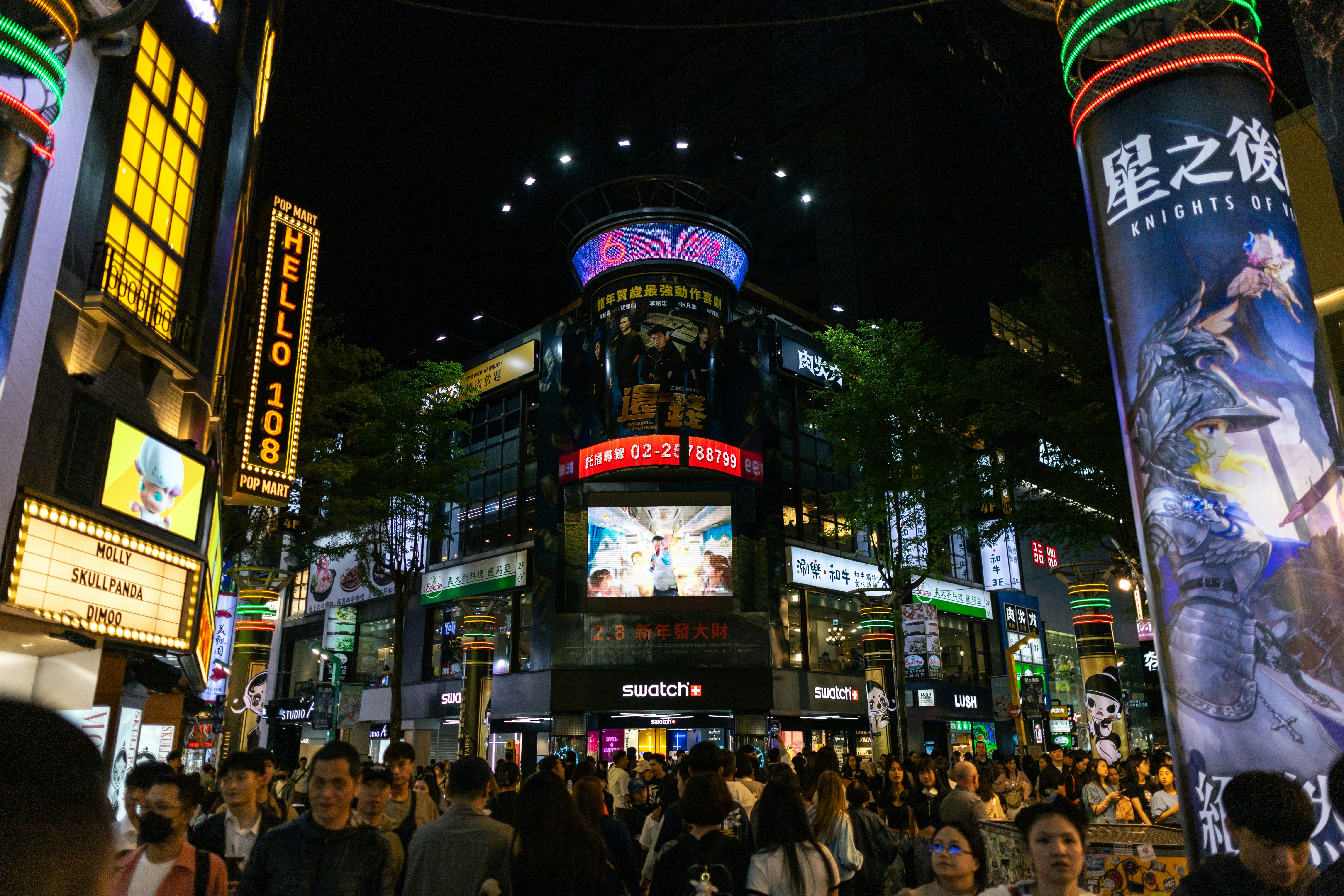 a crowd of people walking around a city at night