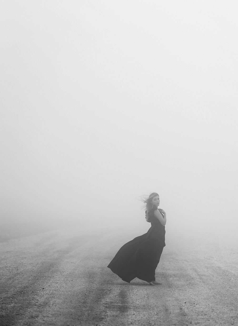 a woman standing in the middle of a road on a foggy day