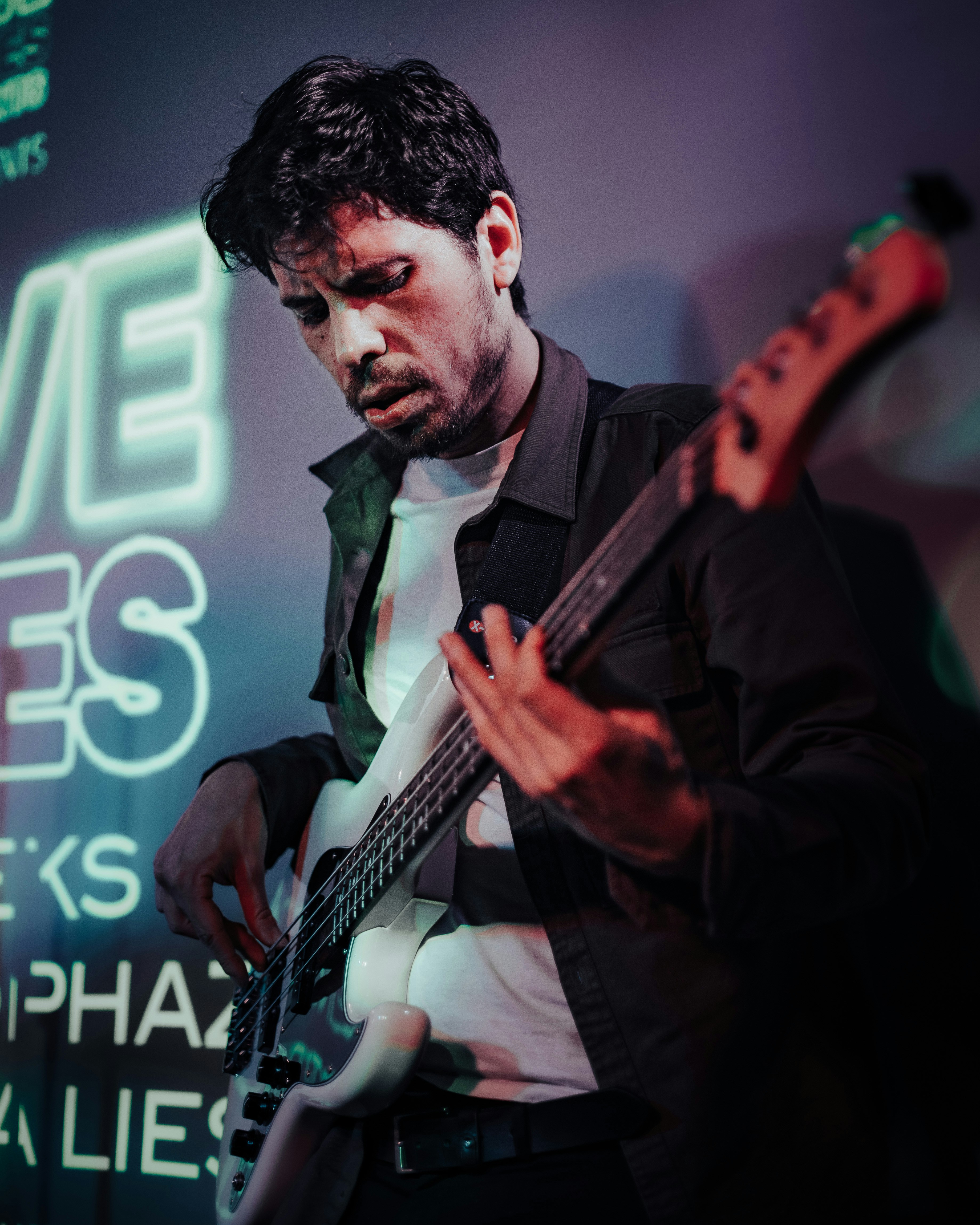 a man playing a bass guitar in front of a neon sign